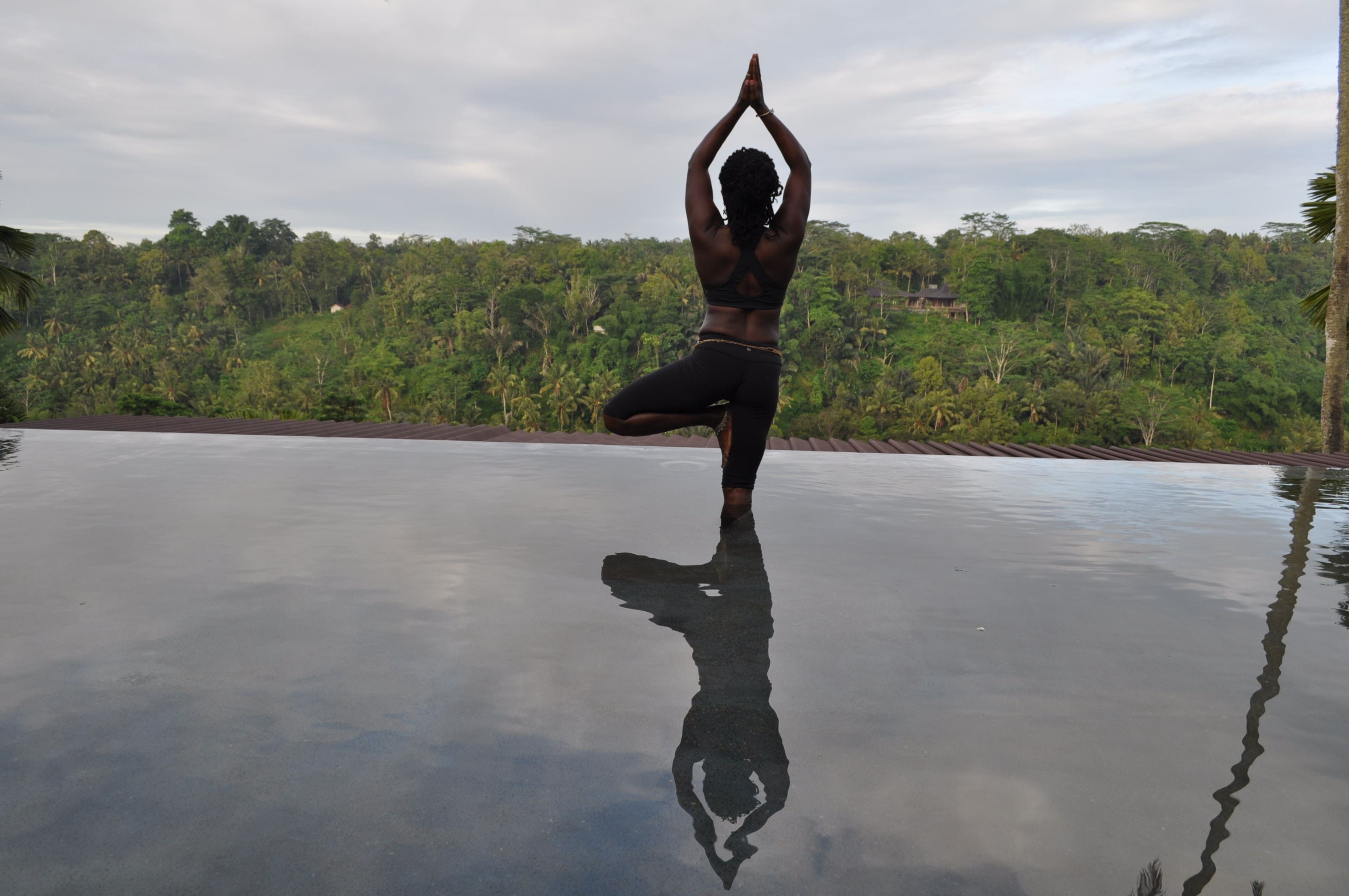 A person is doing yoga on the edge of a pool.