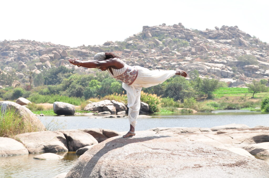 A woman is doing yoga on the rocks by the water.