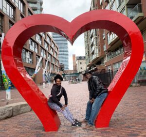 Two people posing in red heart sculpture.