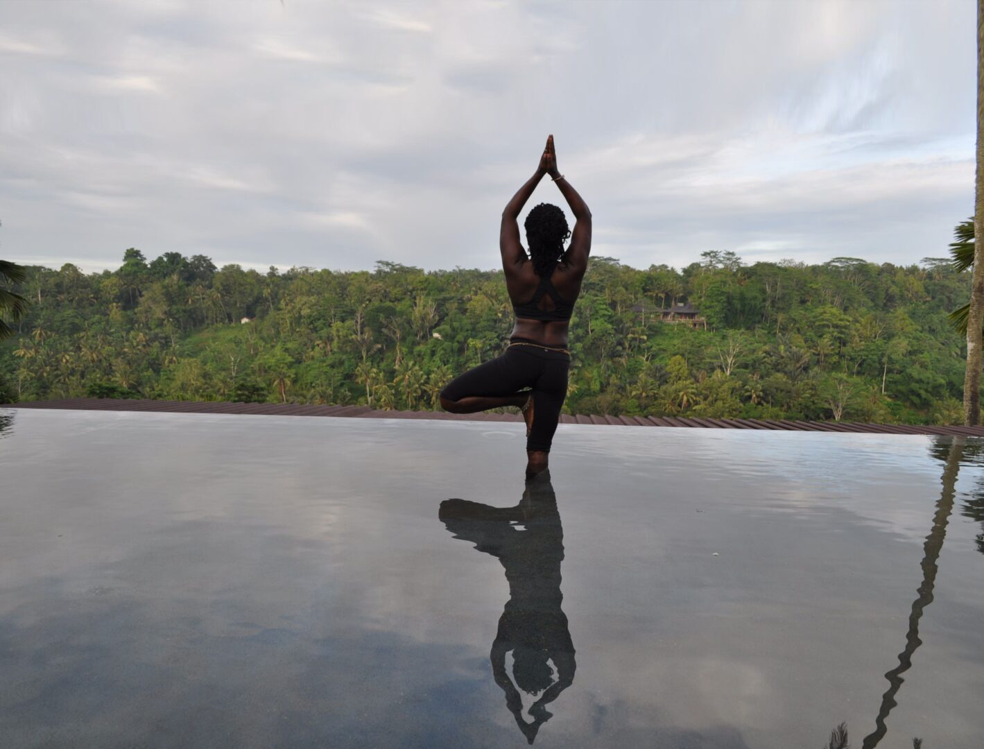 A person is doing yoga on the edge of a pool.