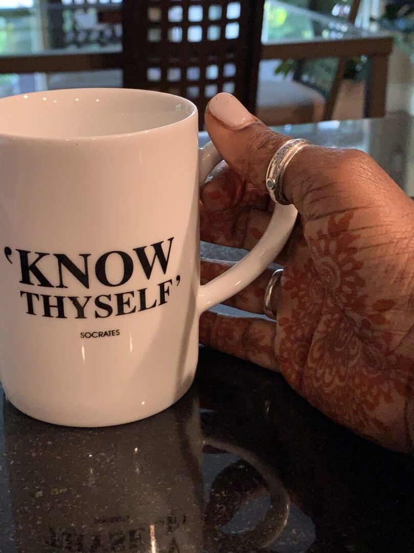 A person holding onto a coffee mug with the words " know thyself ".